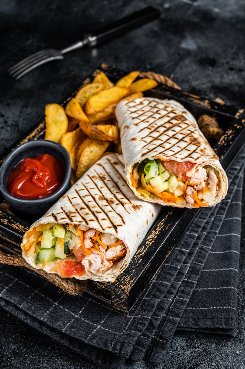 Durum doner kebab or Shawarma with meat, vegetable salad and french fries. Black background. Top view